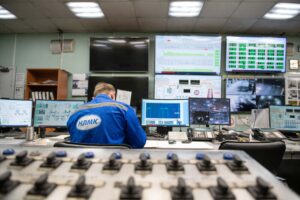 Ingeniero supervisando múltiples pantallas de monitorización en una sala de control industrial moderna, mostrando datos de producción y procesos en tiempo real
