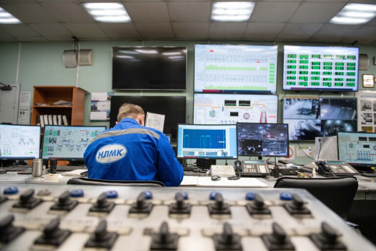 Ingeniero supervisando múltiples pantallas de monitorización en una sala de control industrial moderna, mostrando datos de producción y procesos en tiempo real