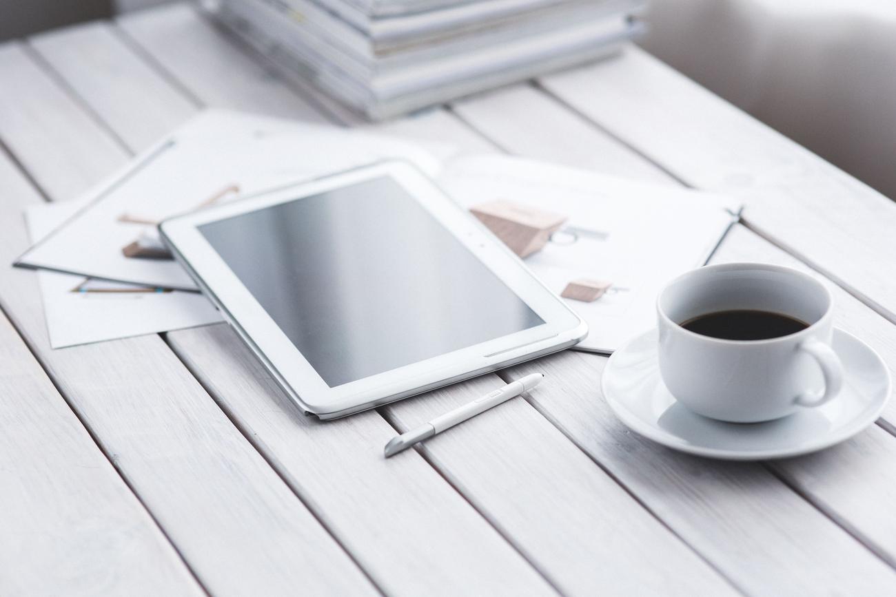 Tablet blanca con lápiz óptico y una taza de café en un escritorio moderno y luminoso Tablet blanca con lápiz óptico y una taza de café en un escritorio moderno y luminoso