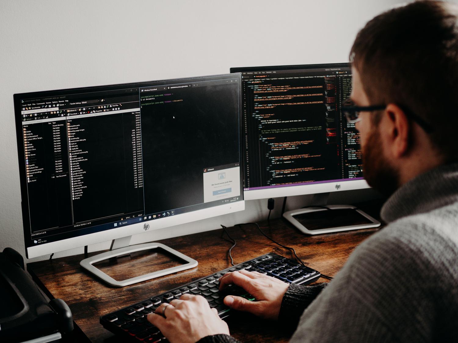 Desarrollador trabajando en licencias de software en monitores duales Desarrollador de software escribiendo código en monitores duales, representando el entorno de creación de licencias.
