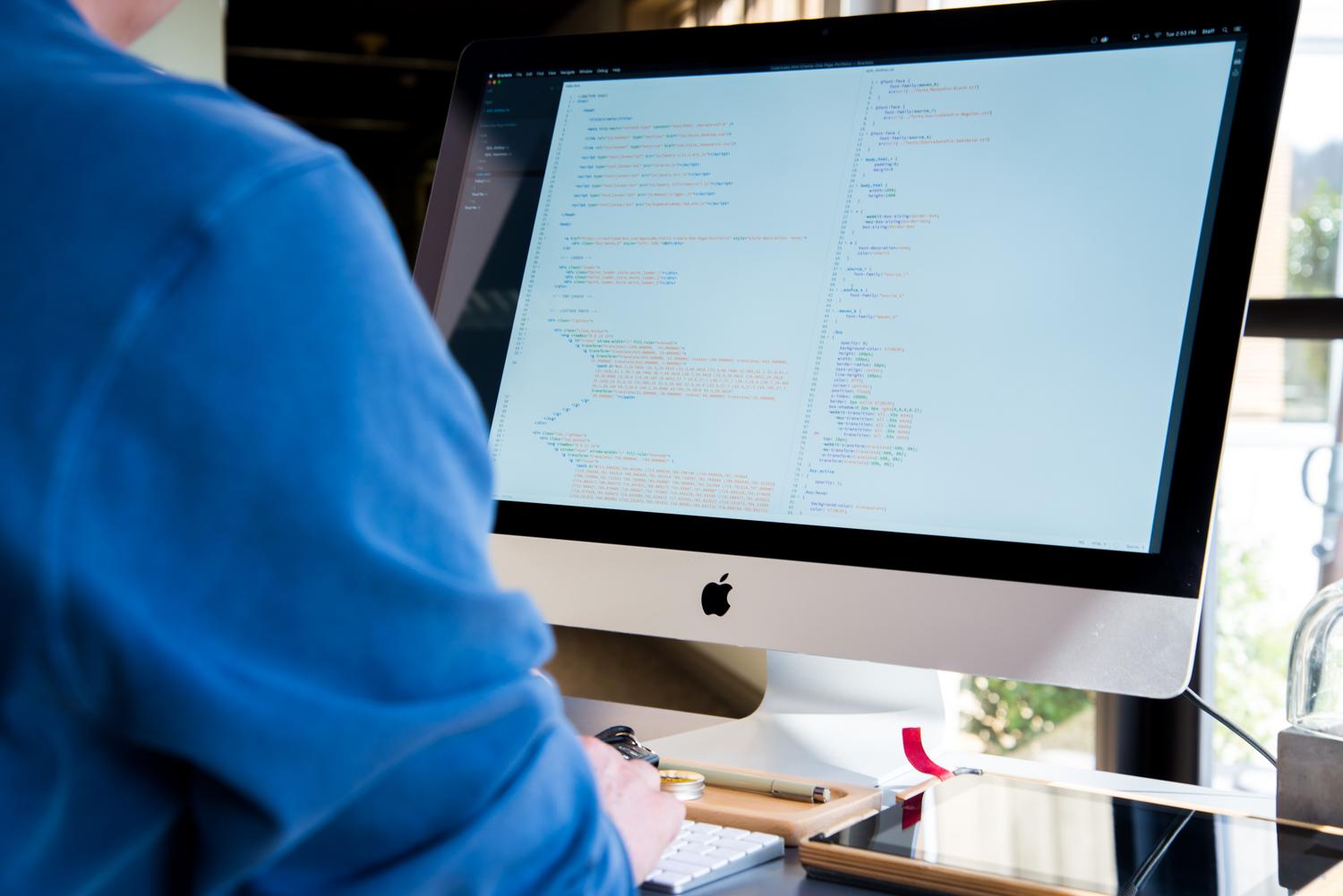 Programador desarrollando software en un ordenador Un programador trabajando en el código de un ordenador iMac, ideal para representar el desarrollo de software.