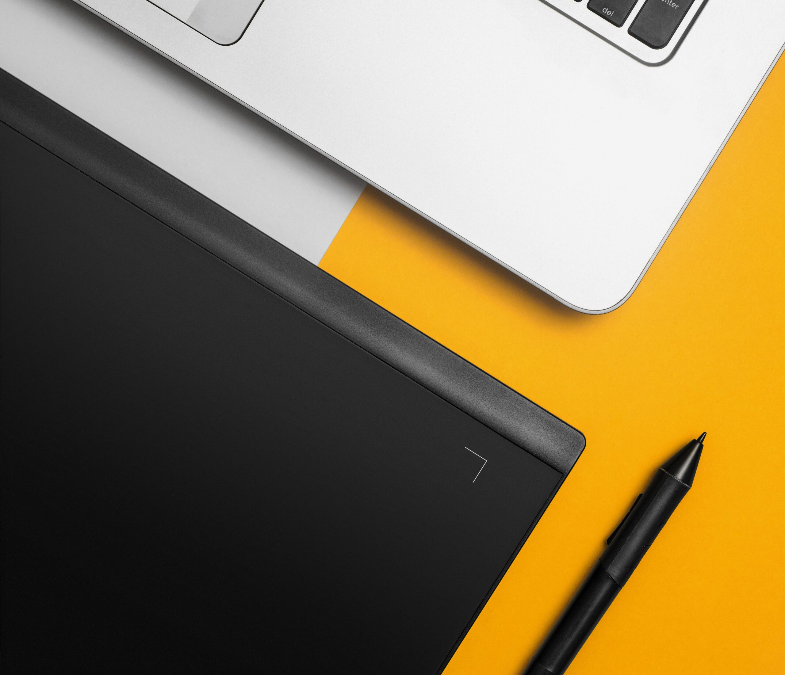 Vista cenital de un espacio de trabajo de diseño gráfico moderno con un ordenador portátil, una tableta digitalizadora y un lápiz óptico sobre un fondo colorido. Vista cenital de un espacio de trabajo de diseño gráfico moderno con un ordenador portátil, una tableta digitalizadora y un lápiz óptico sobre un fondo colorido.