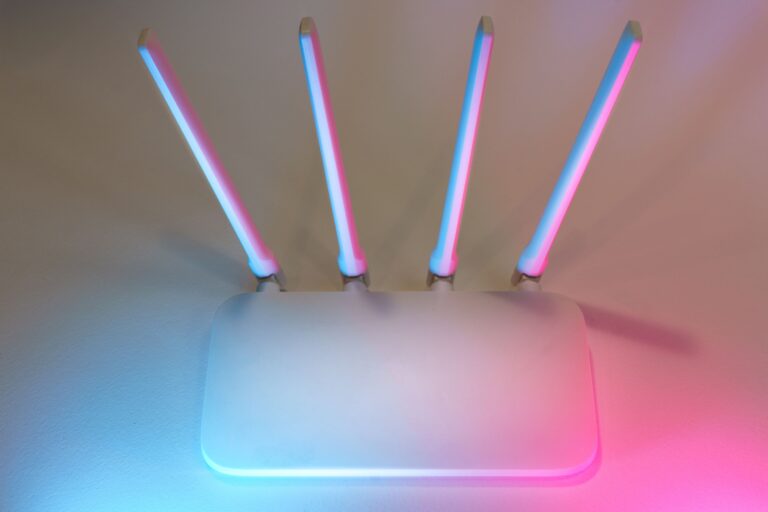 Router inalámbrico moderno de color blanco con cuatro antenas externas emitiendo luz azul y rosa, mostrando los componentes externos del dispositivo de red doméstico