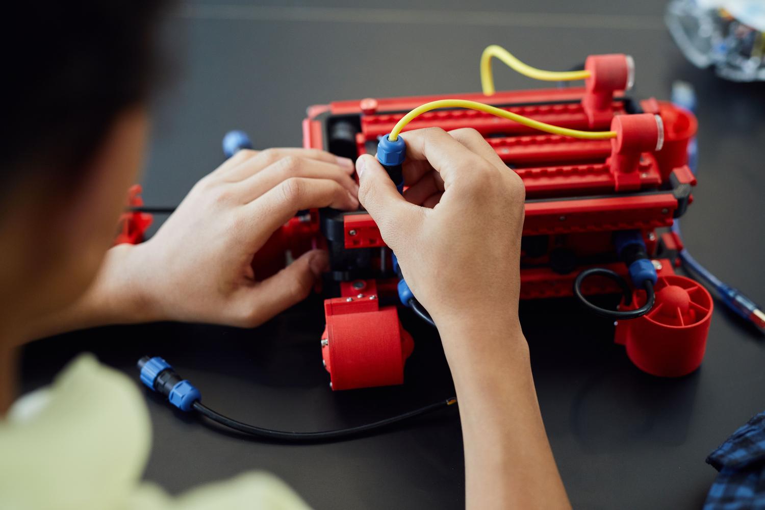 Detalle de las manos de un estudiante ensamblando cables y componentes electrónicos de un robot. Detalle de las manos de un estudiante ensamblando cables y componentes electrónicos de un robot.