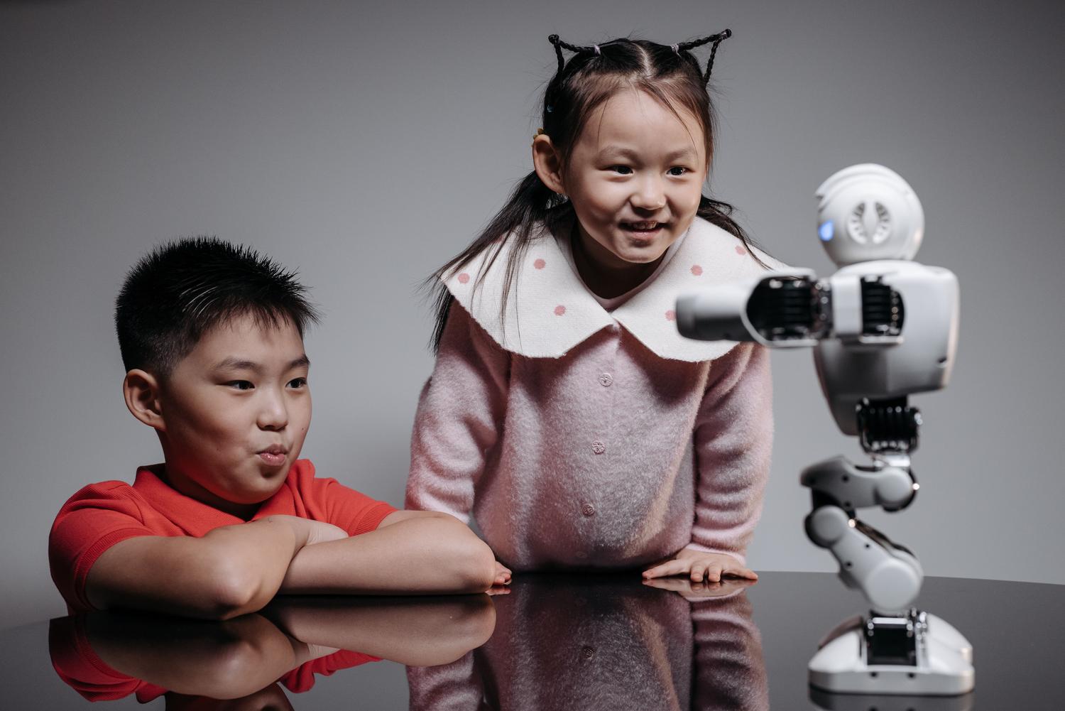 Dos niños interactuando con un pequeño robot educativo en una mesa, fomentando la curiosidad y el aprendizaje STEM. Dos niños interactuando con un pequeño robot educativo en una mesa, fomentando la curiosidad y el aprendizaje STEM.