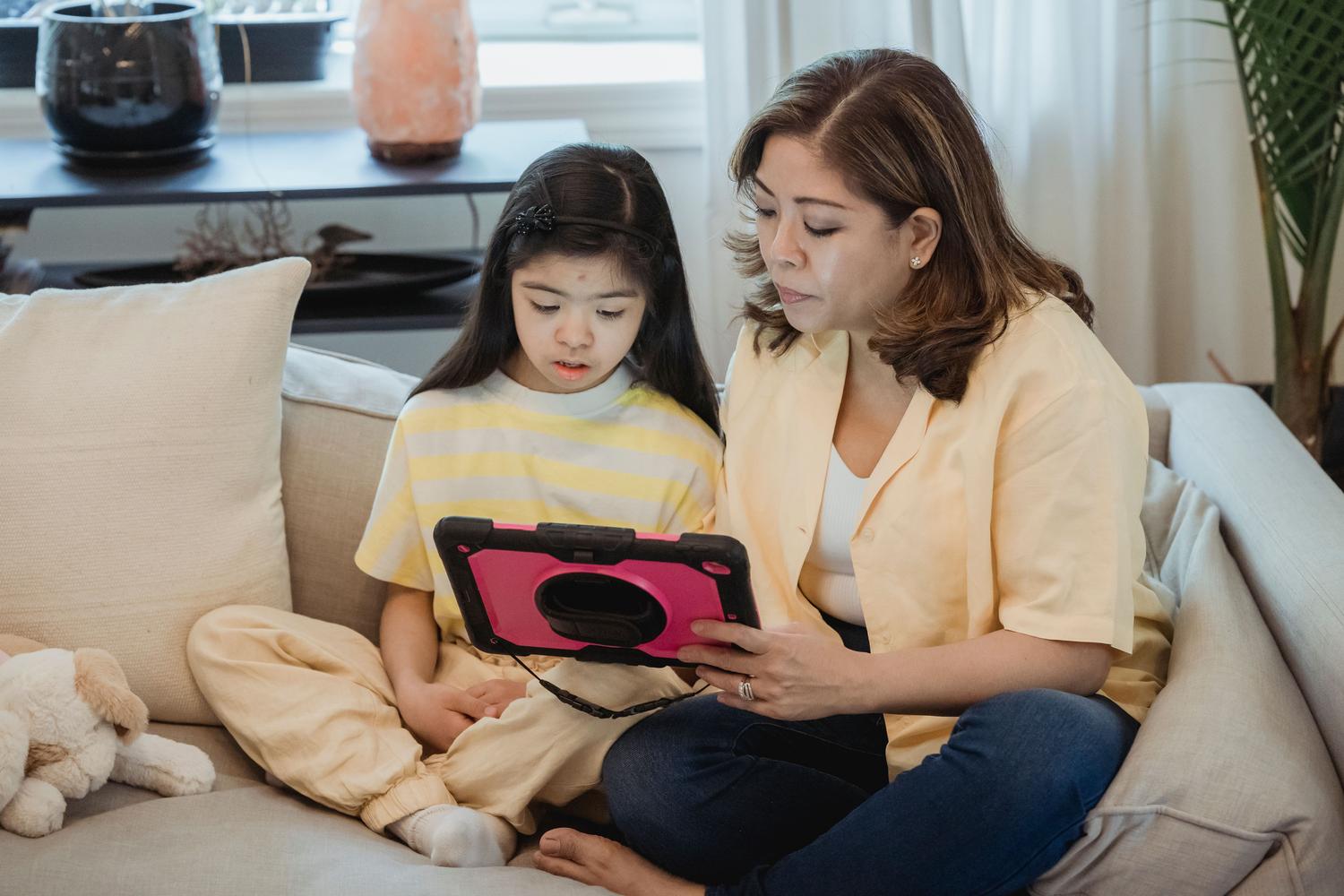 Madre y niña interactuando con una tablet en el sofá, representando la supervisión natural y el tiempo de calidad. Madre y niña interactuando con una tablet en el sofá, representando la supervisión natural y el tiempo de calidad.