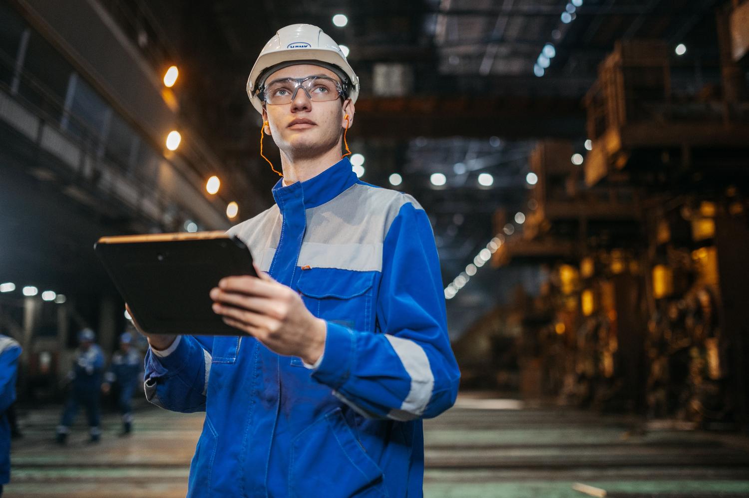 Operario industrial utilizando una tablet para acceder a instrucciones de trabajo digitales en una fábrica moderna Operario industrial utilizando una tablet para acceder a instrucciones de trabajo digitales en una fábrica moderna