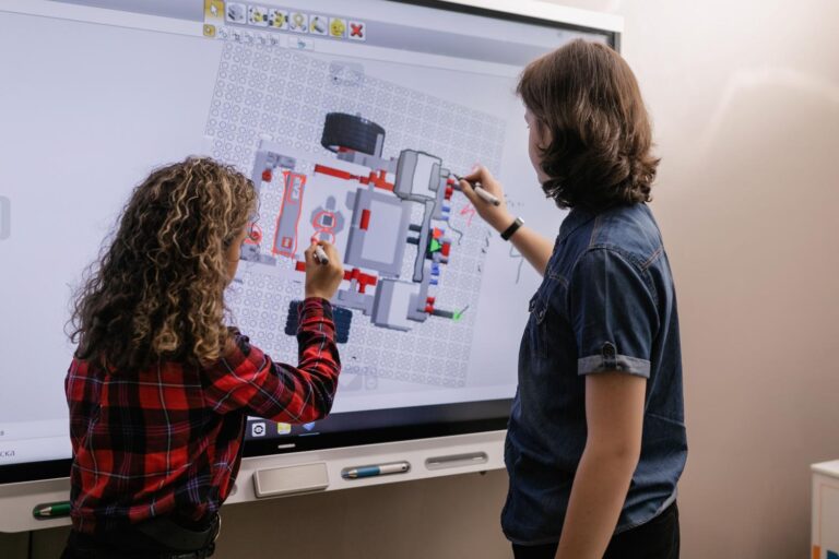 Dva učenika komuniciraju s digitalnom pločom u modernoj učionici koristeći obrazovni softver za robotiku.