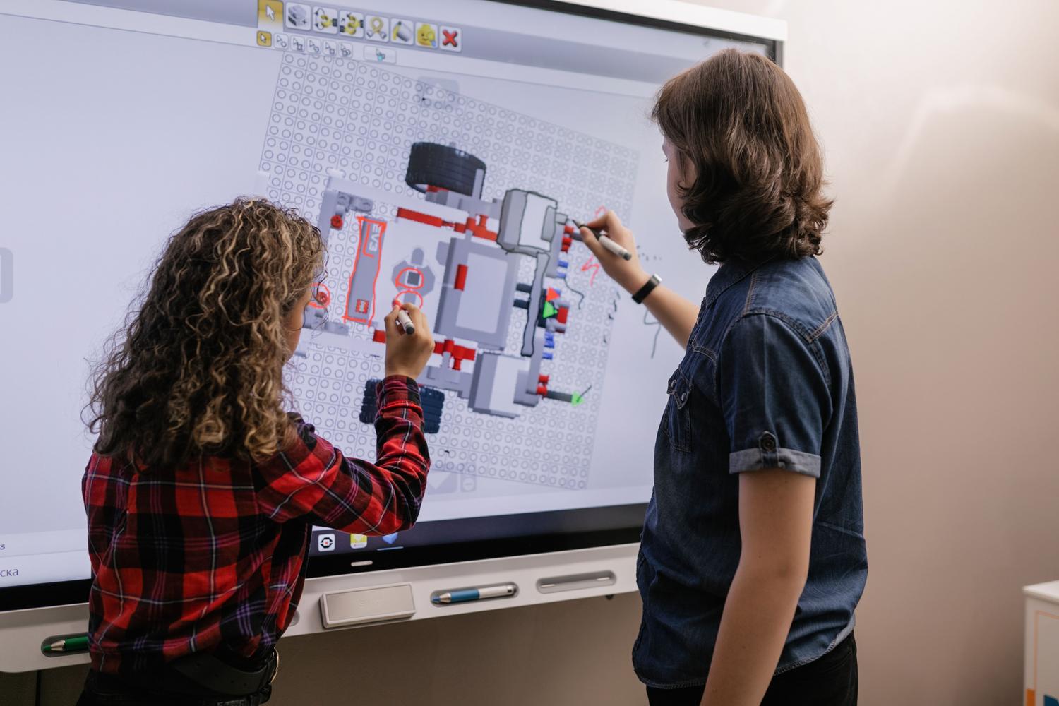Dos estudiantes interactuando con una pizarra digital en un aula moderna, utilizando software de robótica educativa. Dos estudiantes interactuando con una pizarra digital en un aula moderna, utilizando software de robótica educativa.