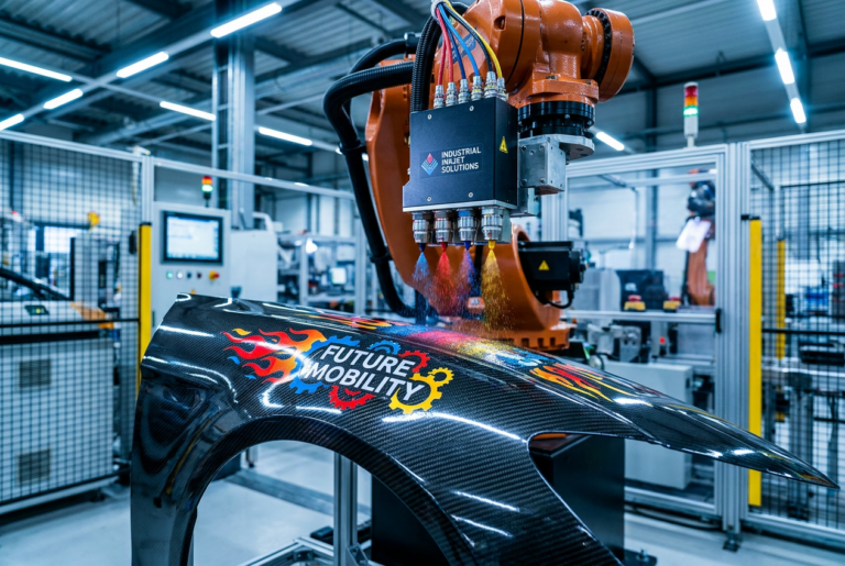 Primer plano de un brazo robótico industrial aplicando una impresión detallada y colorida sobre una pieza automotriz curva, ilustrando la tecnología de impresión direct-to-shape.