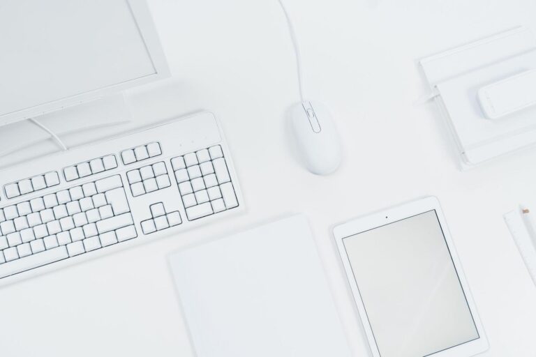 Espacio de trabajo minimalista con teclado, ratón y tableta blanca sobre un escritorio moderno.