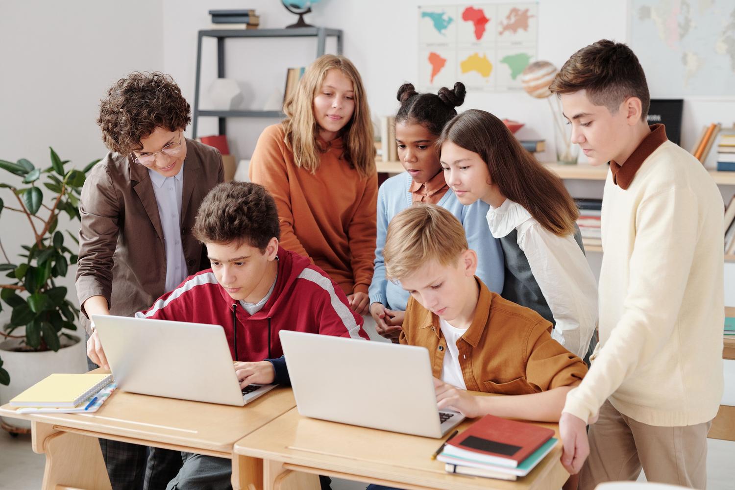 Programación avanzada para adolescentes Adolescentes trabajando en equipo con laptops en un entorno escolar para desarrollar proyectos de programación avanzada.
