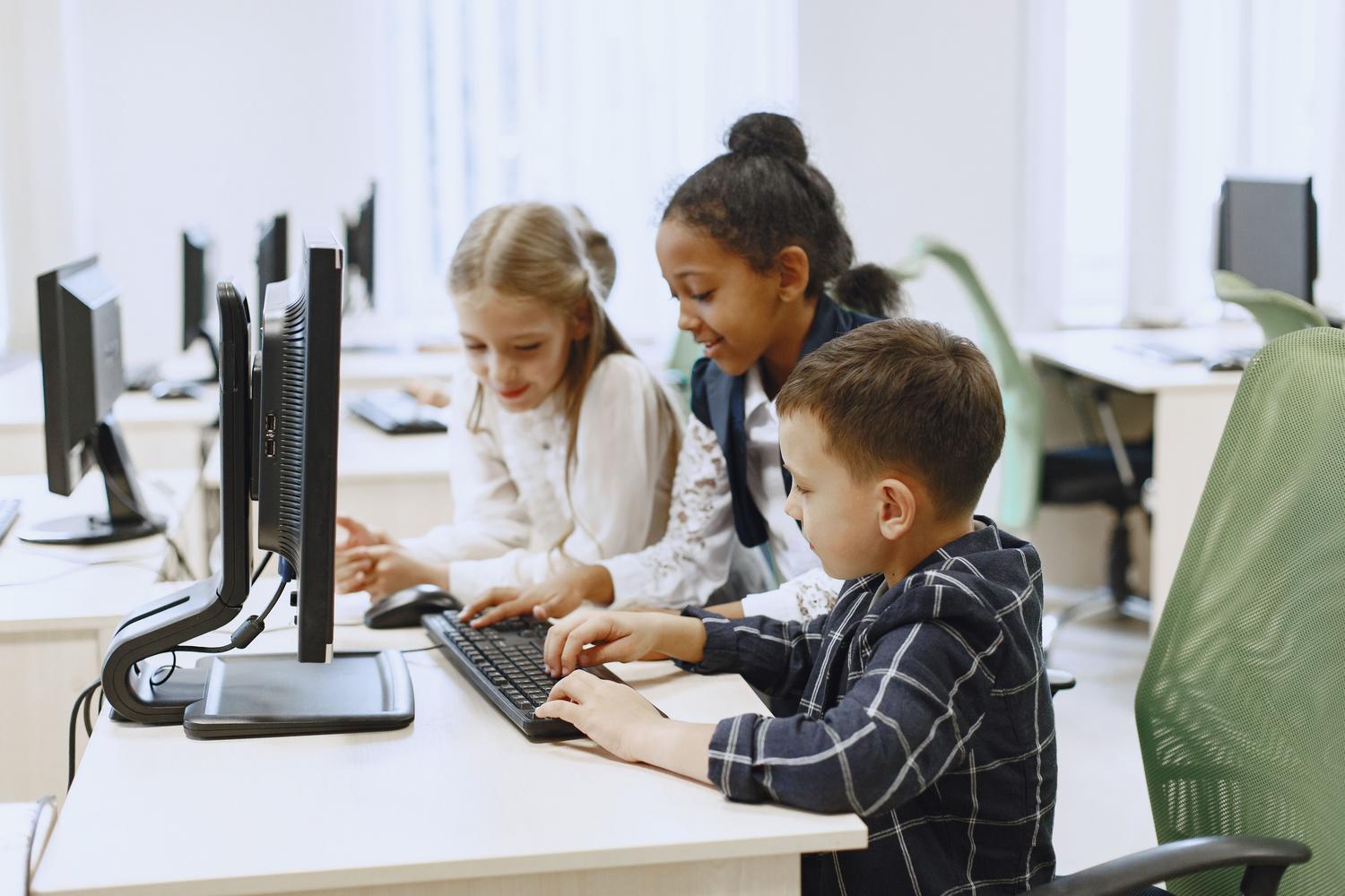 Programación para niños y adolescentes Niños colaborando alegremente en un laboratorio de informática aprendiendo los conceptos básicos de programación.