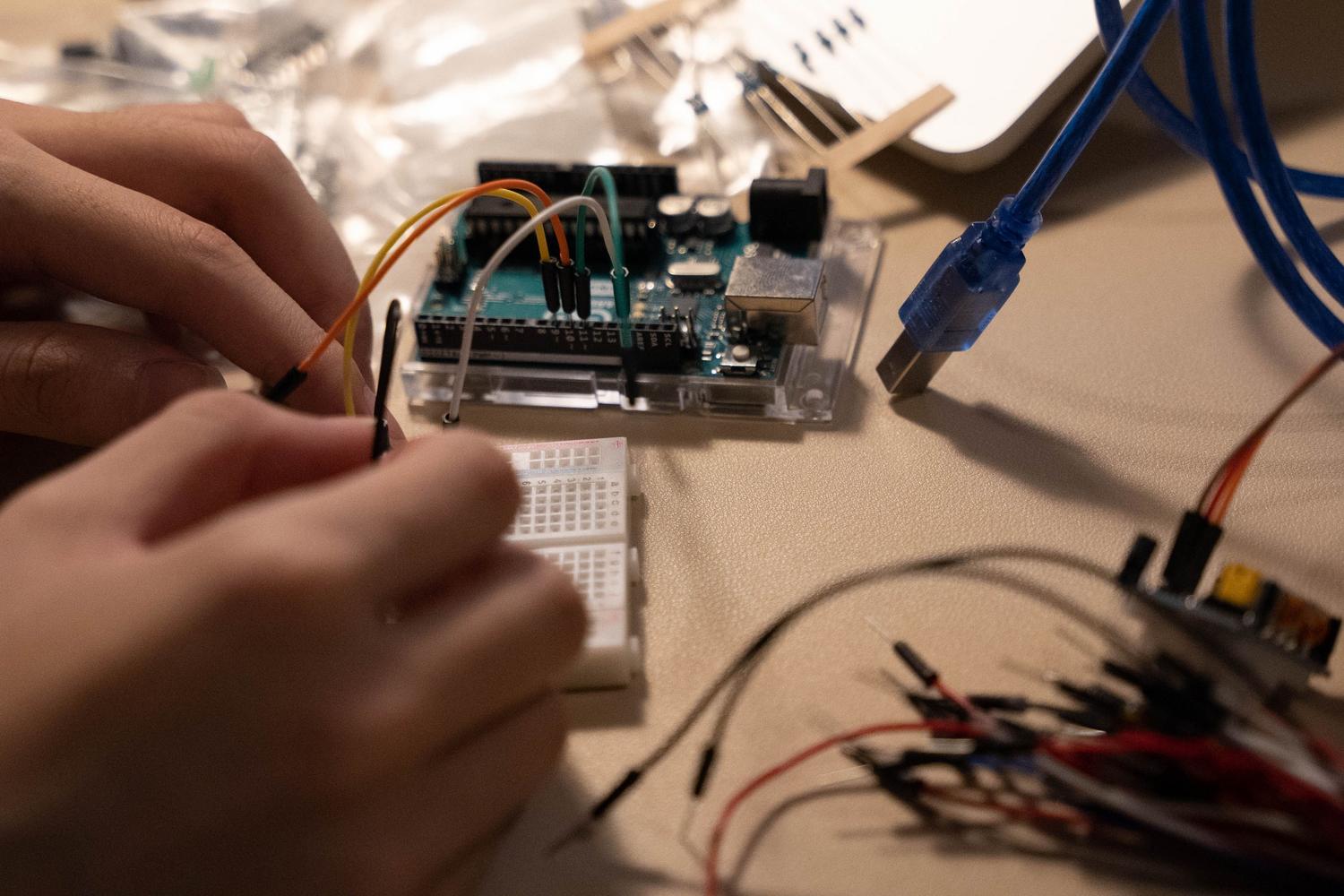 Manos ensamblando componentes electrónicos y cables en una protoboard, ideal para ilustrar la sección de puesta en marcha y entorno de desarrollo. Manos ensamblando componentes electrónicos y cables en una protoboard, ideal para ilustrar la sección de puesta en marcha y entorno de desarrollo.